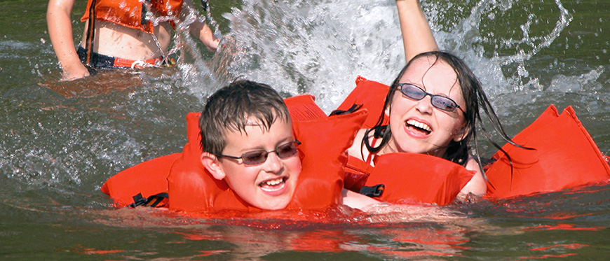 Kids swimming in lake with orange life jackets