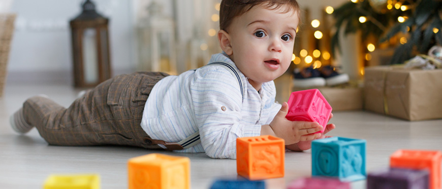 Toddler boy playing with plastic blocks in front of Christmas Tree