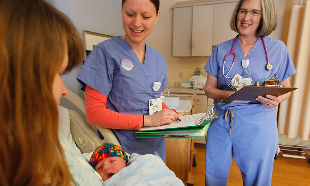 Two nurses gathering information from new mom holding her baby